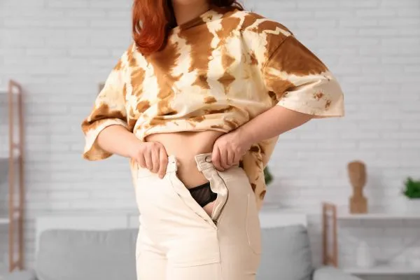 Image of woman trying to do her trousers up after pregnancy weight gain Newport